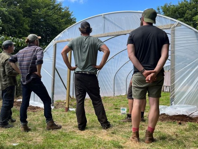 Four men facing towards a newly-erected poly tunnel