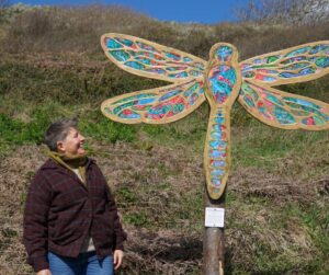 An older person stands looking up and smiling at one of the dragonfly sculptures along the art rail.