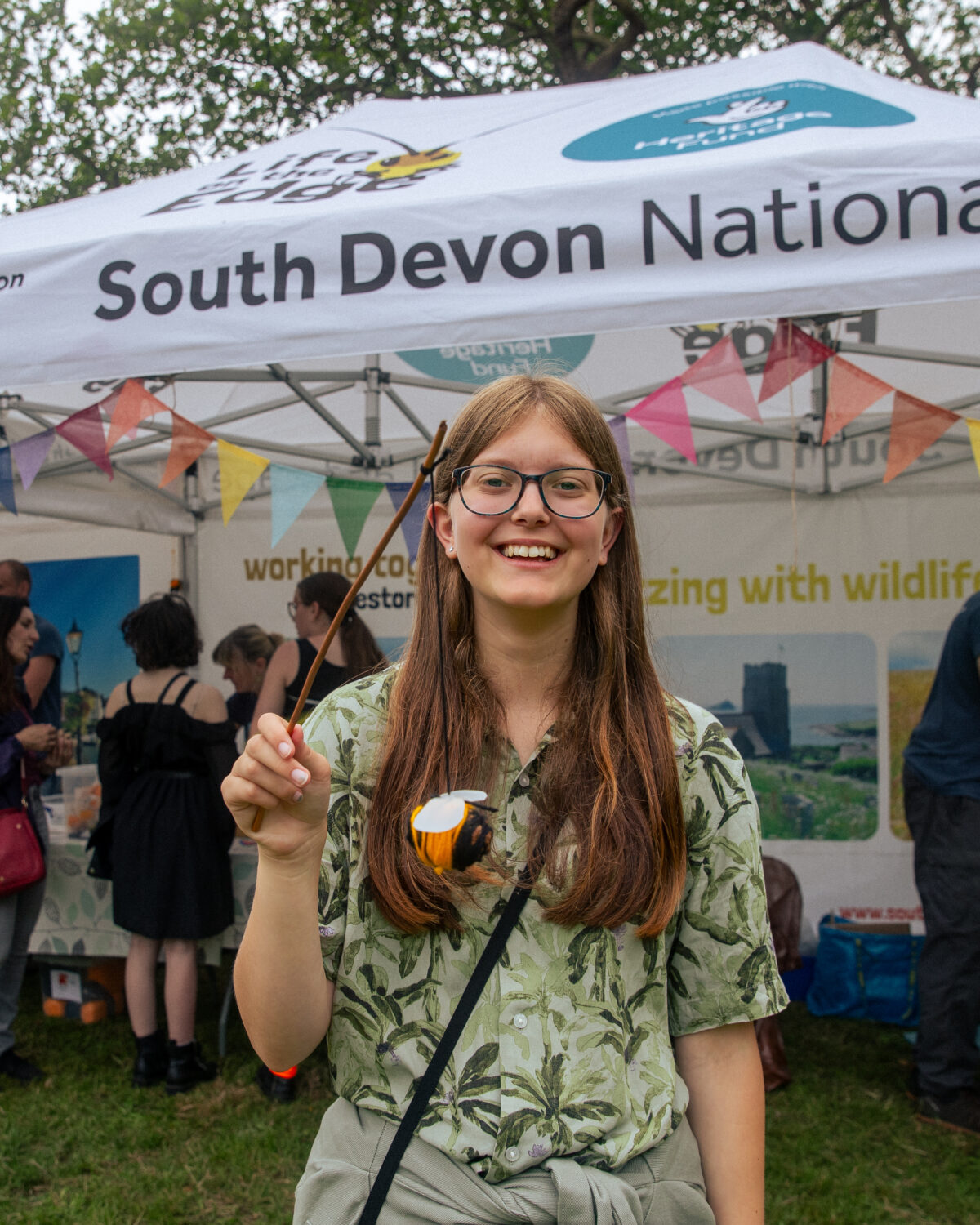 A picture of a young person smiling and holding a felt bee they have made.