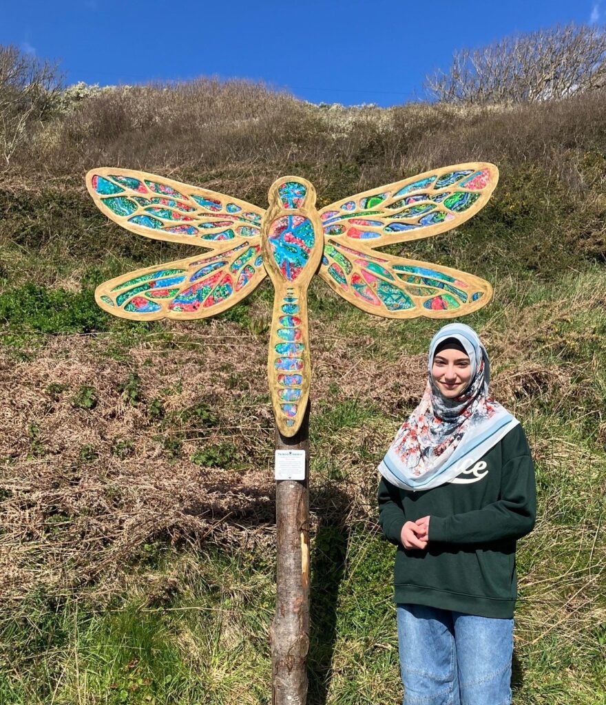 A young person standing beside one of the dragonfly sculptures