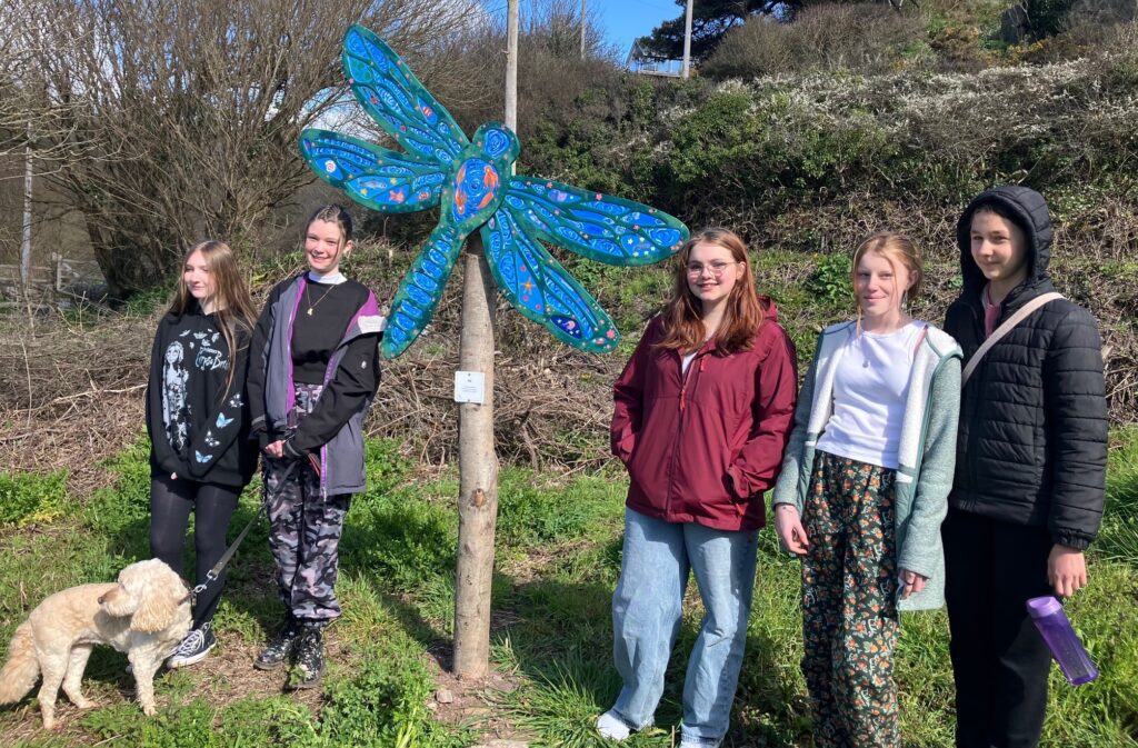 A group of young people proudly surrounding the newly-installed dragonfly that they painted