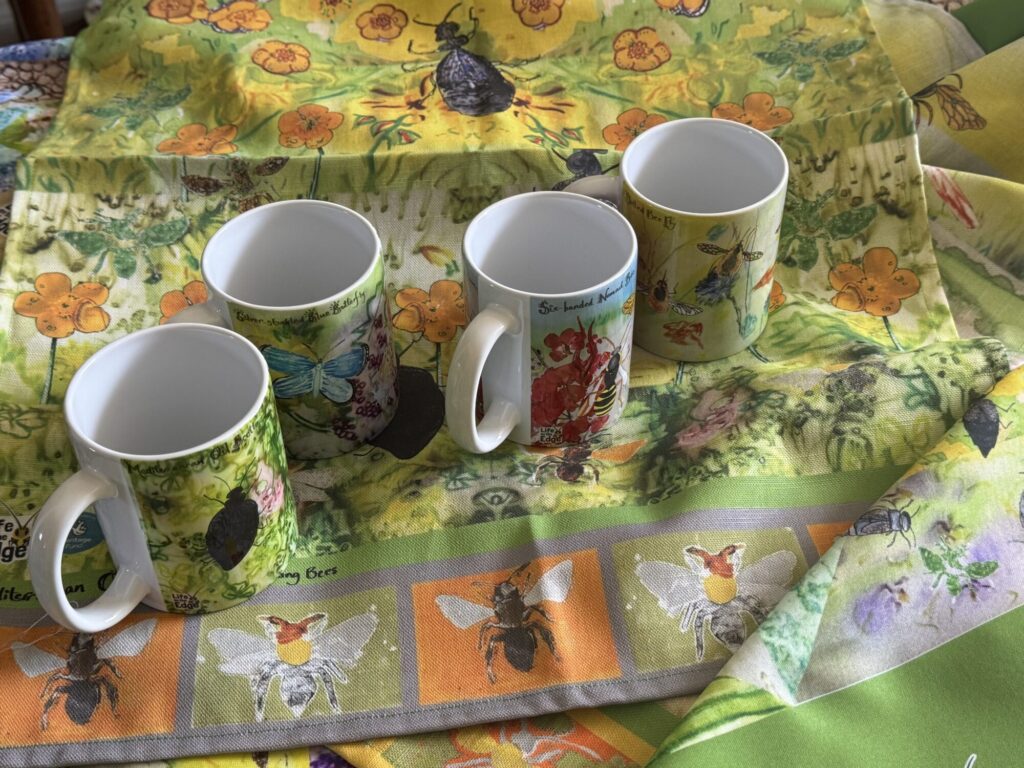 Some mugs and a tea towel on a table cloth, all designed by the participants of this project