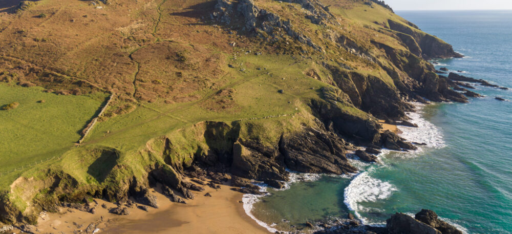 view down onto sandy cove with hill and rock outcrops rising up the other side of the beach
