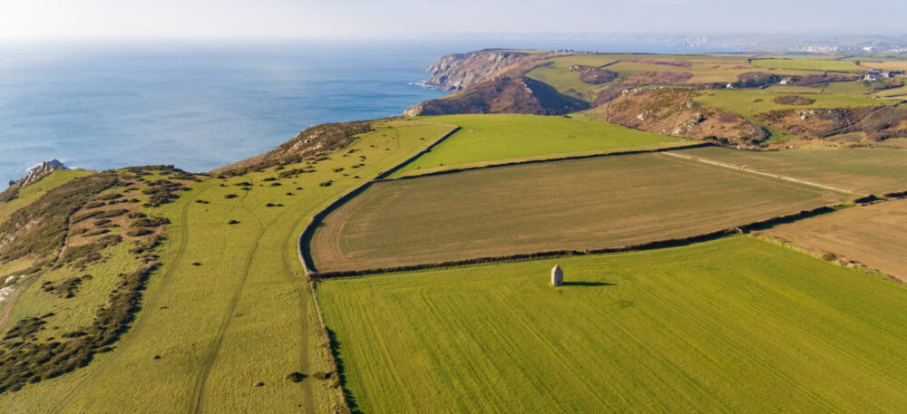 ariel view across fields on coast and out to sea. stone tower in foreground field
